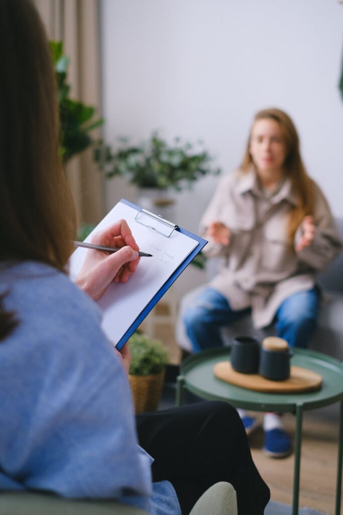 Photo by SHVETS production Unrecognizable female psychologist taking notes on clipboard while listening to patient sitting on blurred background during psychotherapy consultation in office